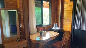 Una habitación de cabaña de madera con una mesa redonda de madera, un espejo, una ventana con cortinas y una mesita con artículos de aseo.