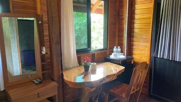 A wooden cabin interior with a dining table, chairs, a small window with curtains, and a mirror.