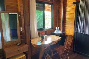 Interior de una cabaña de madera con una mesa de comedor, sillas, una ventana pequeña con cortinas y un espejo.