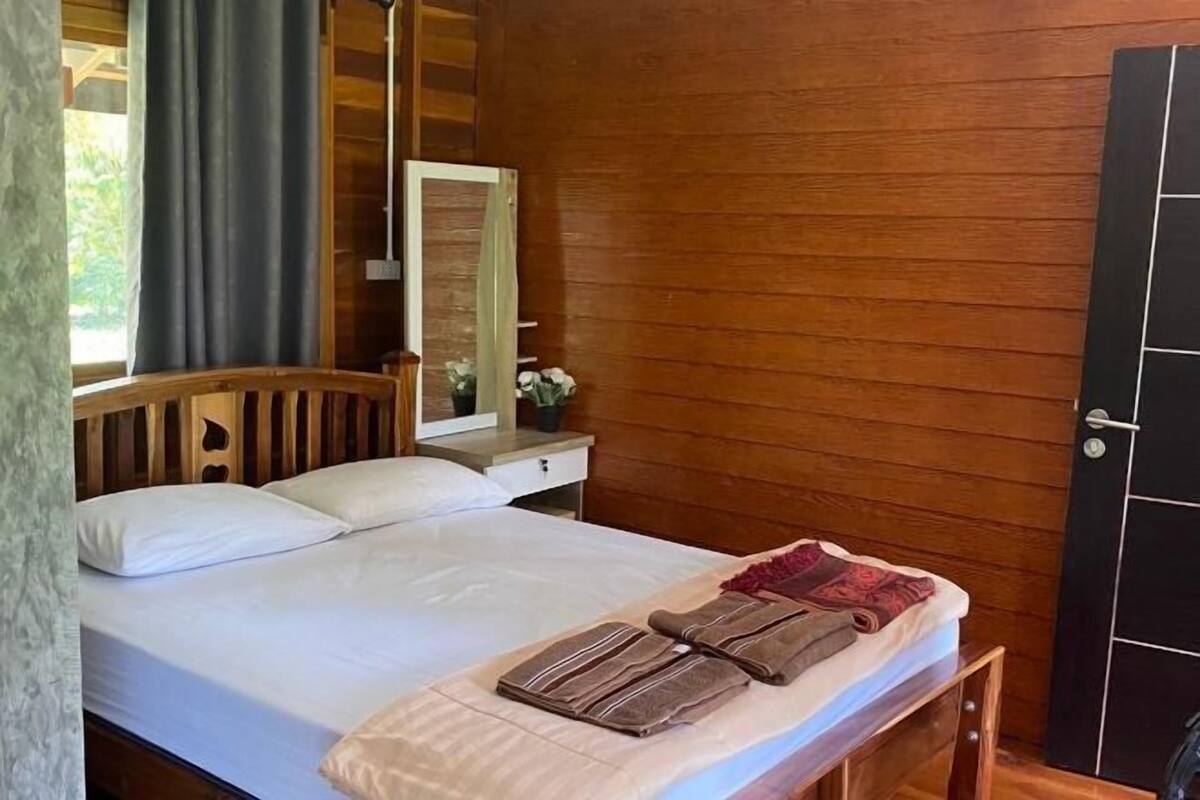 A wooden-paneled room with a bed, a bedside table, a mirror, and a door.