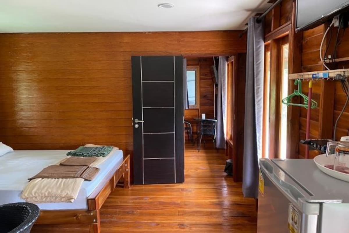 A wooden-paneled room with a bed, a small table, and a kitchenette area.