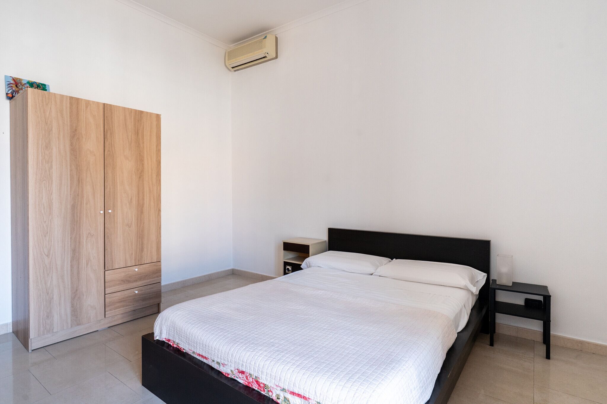 Ein Schlafzimmer mit Bett, Kleiderschrank, Nachttisch und einer Wand-Klimaanlage.