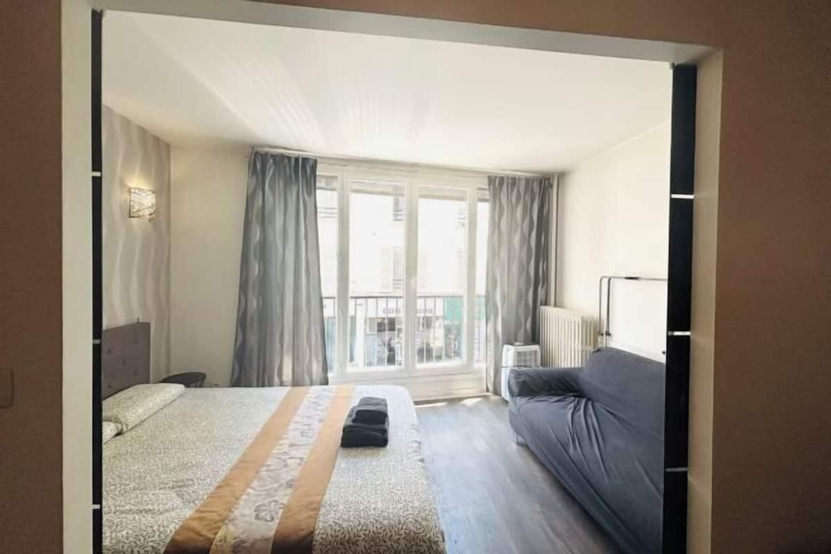 A hotel room with a bed, a sofa, a window with curtains, and a radiator.