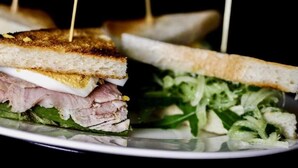 A sandwich with toothpicks, meat, cheese, and greens on a plate. - Pension Haus Marianne (Nußdorf ob der Traisen)