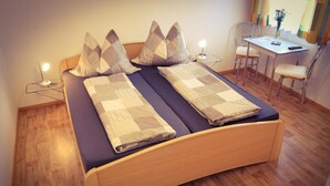 A double bed with patterned bedding, bedside lamps, a small table with a chair, and a desk with a chair. - Pension Haus Marianne (Nußdorf ob der Traisen)
