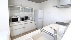Een moderne keuken met witte kastjes, een magnetron, een koffiezetapparaat en een koelkast.