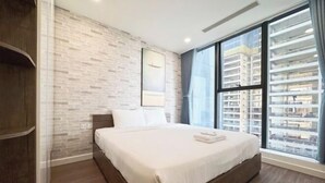 Un dormitorio moderno con una cama grande, una pared con diseño de ladrillo, una ventana con vistas a edificios y un armario de madera.