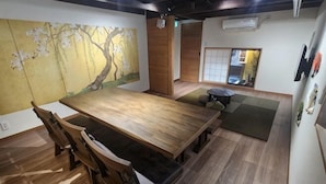 Un coin repas avec une table et des chaises en bois, un tatami et une peinture japonaise traditionnelle accrochée au mur.