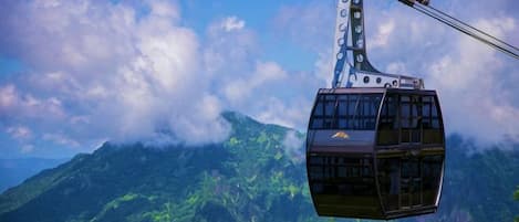 A cable car suspended over a mountainous landscape with lush greenery and clouds.