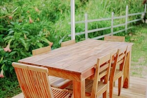 A wooden table and chairs set outdoors with a white fence and greenery in the background.