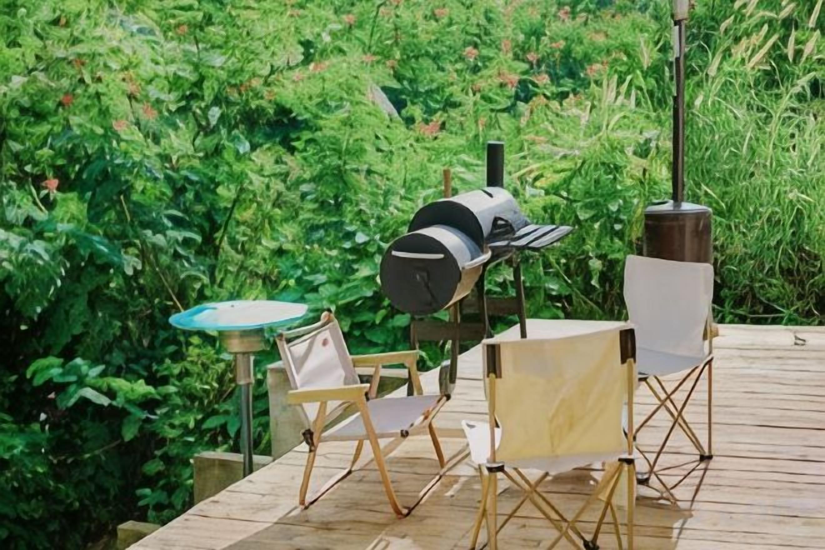 An outdoor deck with a grill, two folding chairs, and a table.