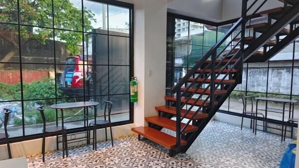 Un escalier avec des marches en bois et des rampes noires, menant à un balcon doté d’un sol carrelé et offrant une vue sur un véhicule garé à l’extérieur.