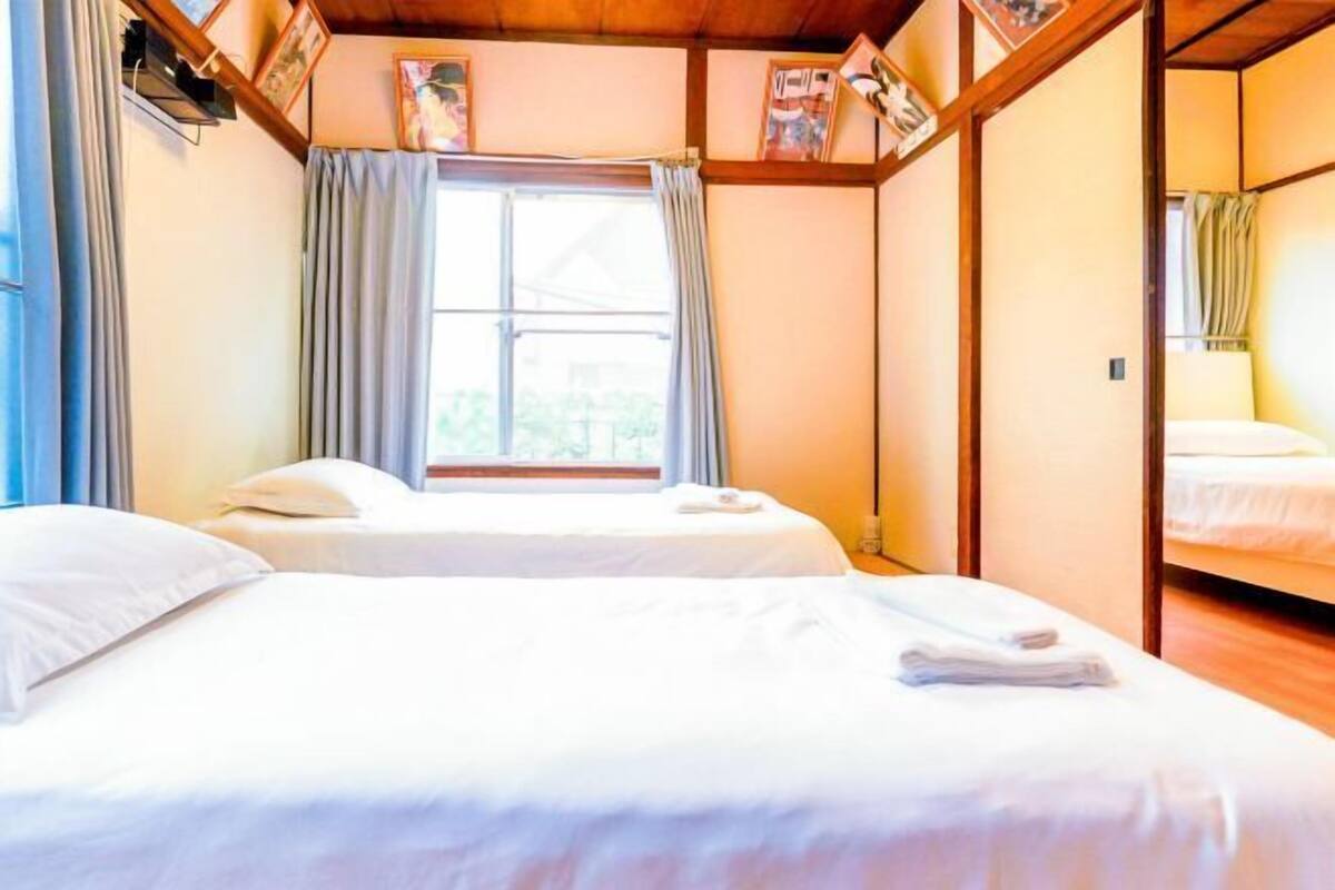 Ein Zimmer mit zwei Betten, einem Vorhangfenster, Holzbalken und gerahmten Bildern an der Wand.