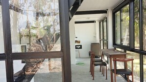 A room with large windows, a dining area with wooden tables and chairs, and a view of trees outside. - farm sam sook (Lamphun)