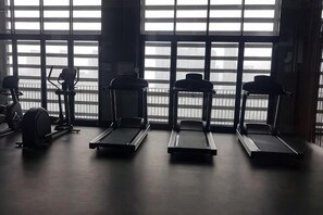 Ein Fitnessraum mit Laufbändern und Crosstrainern, großen Fenstern und Blick auf die Stadt.
