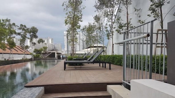 Un espace piscine aménagé sur le toit, avec des marches descendant vers l’eau, entouré d’arbres et bordé de bâtiments modernes en arrière-plan.