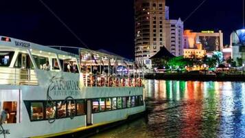 A river cruise boat with a dining area and a view of a city skyline at night.