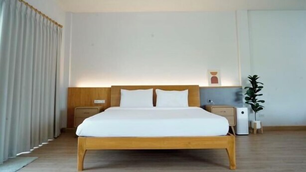 A modern hotel room with a wooden bed, two bedside tables, a nightstand, a wall-mounted light, and a potted plant. - Lapin No.8 (Chiang Mai)