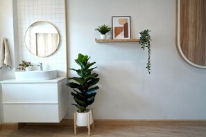 Ein Badezimmer mit einem runden Spiegel, einem weißen Waschbecken, einer Topfpflanze und einem Holzboden.