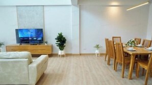 A modern living room with a flat-screen TV, a sofa, a dining table with chairs, and two potted plants. - Lapin No.8 (Chiang Mai)