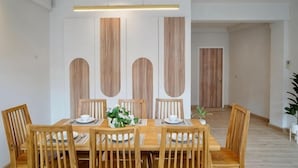 A dining area with a wooden table and chairs, a vase with flowers, and a wooden partition with vertical panels. - Lapin No.8 (Chiang Mai)
