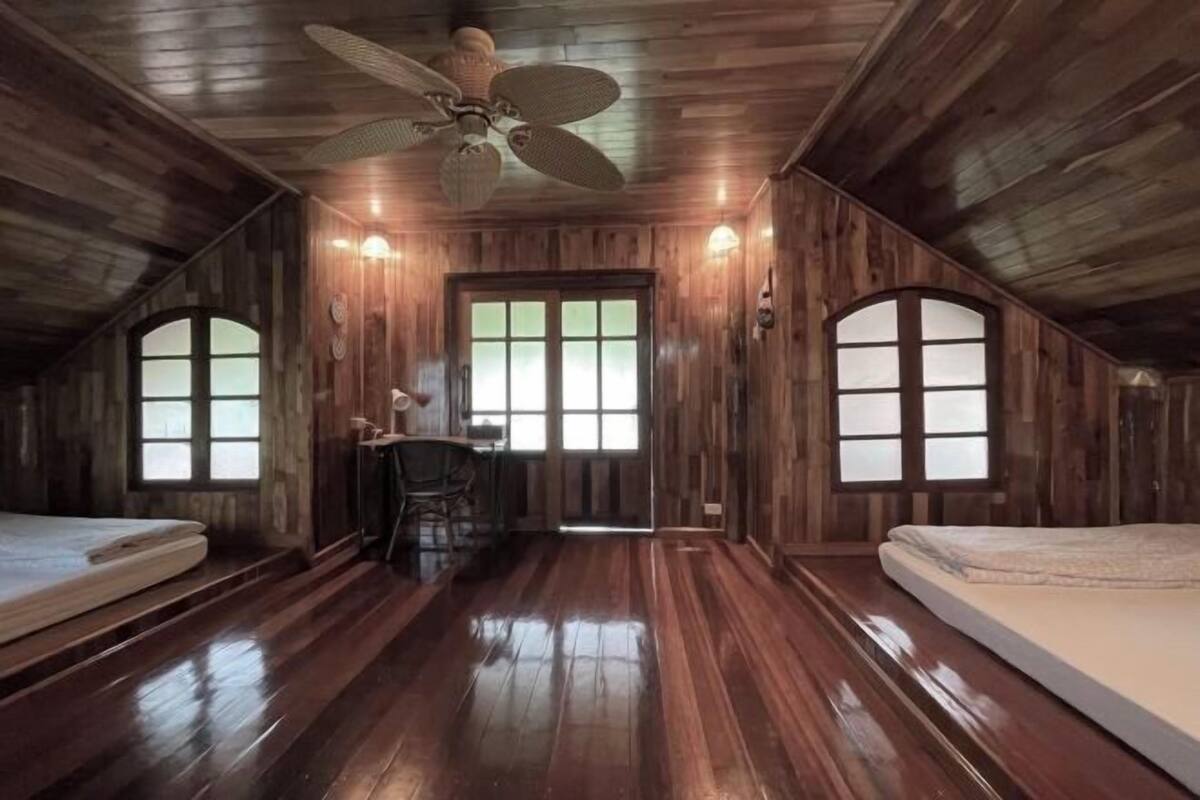 Een kamer met houten wanden, een plafondventilator, een bureau en twee bedden.