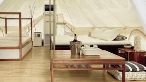 Eine Zelthütte mit Bett, Tisch, Eimer und einer kleinen Sitzecke.