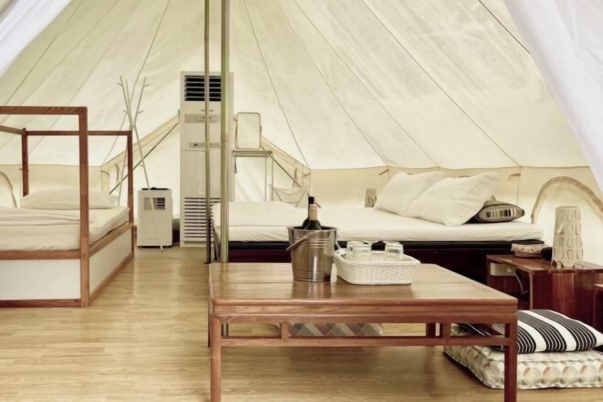 Een tentaccommodatie met een bed, een tafel met emmer, en een klein zitgedeelte.