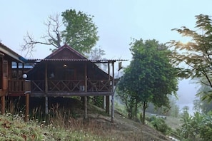 Una cabaña de madera con balcón, rodeada de árboles y un paisaje montañoso.