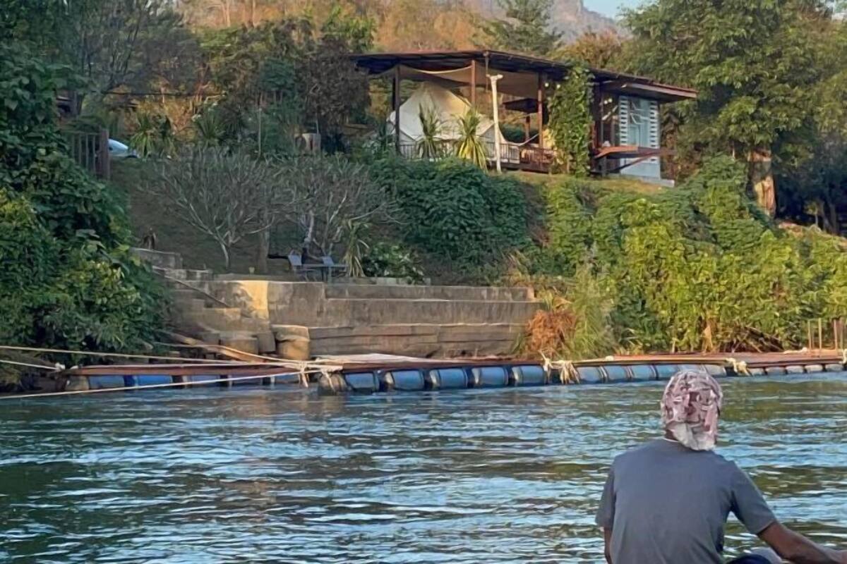 Een man roeit in een boot op een rivier, omringd door weelderige begroeiing en een klein huis op een heuvel.