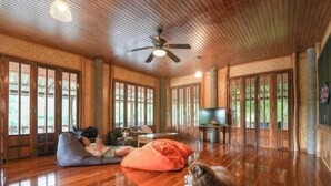 Ein geräumiges Zimmer mit Holzböden, großen Fenstern, einem Deckenventilator und einem Fernseher.