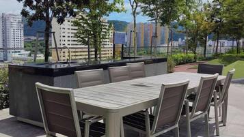 Uma área de refeições ao ar livre com mesa, cadeiras e um bar embutido, oferecendo vista para a cidade.