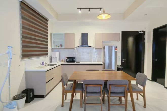 A modern kitchen with a central island, a dining table with chairs, and a black door.