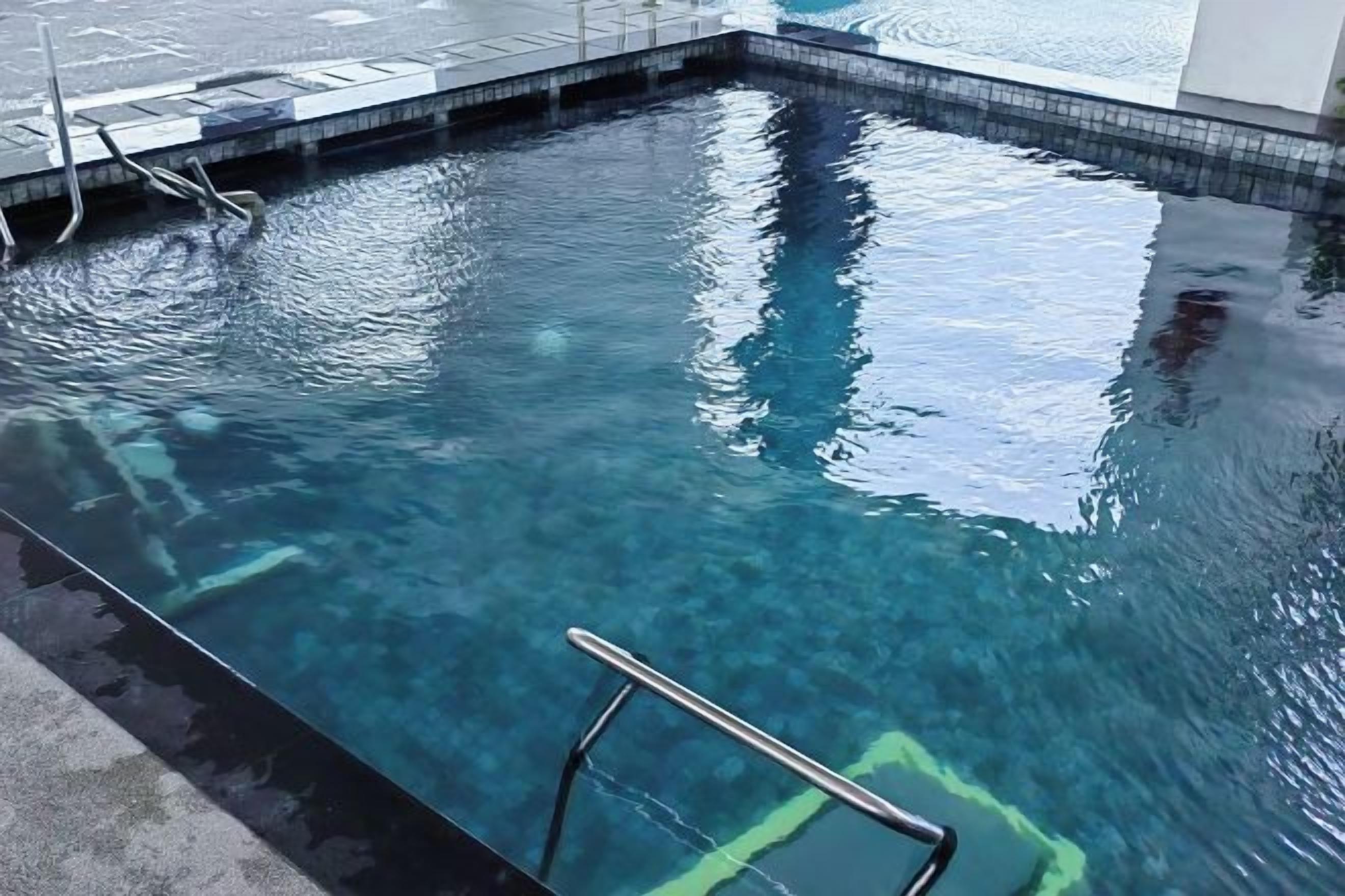 A swimming pool with clear water, a metal ladder, and a tiled edge.