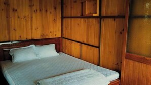 Una habitación de madera con una cama, paredes de madera y un estante pequeño de madera.