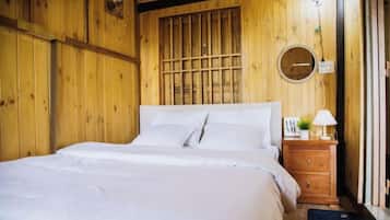 Una habitación de madera con una cama, una mesita de noche y un ventanal con barrotes.