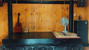 Una habitación de madera con una guitarra, un osito de peluche, un ventilador y un refrigerador pequeño.