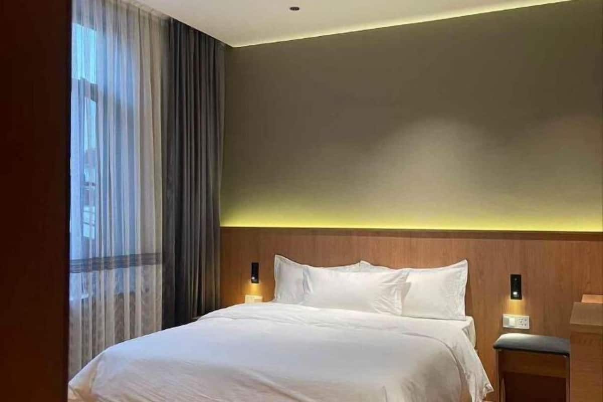 Une chambre d’hôtel avec un lit, des rideaux, une table de chevet et des lampes fixées au mur.