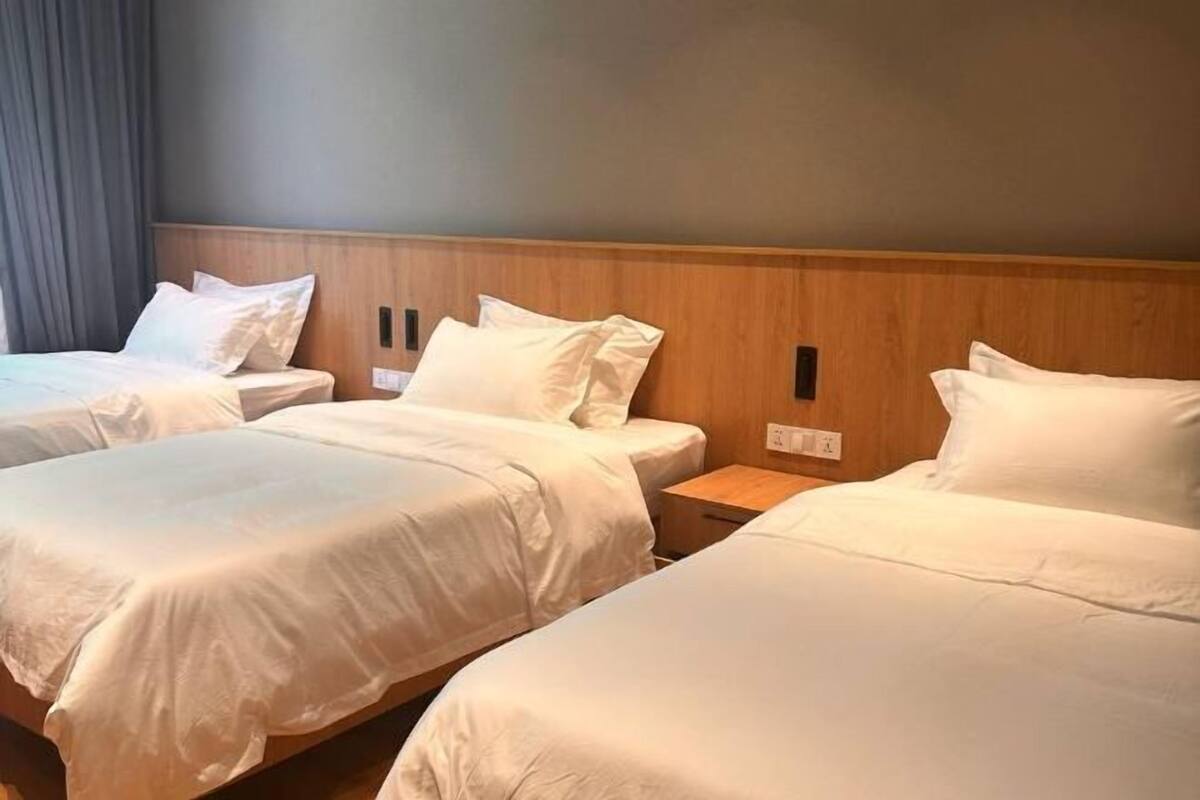 Une chambre d’hôtel avec trois lits simples, une tête de lit en bois et une décoration aux couleurs neutres.