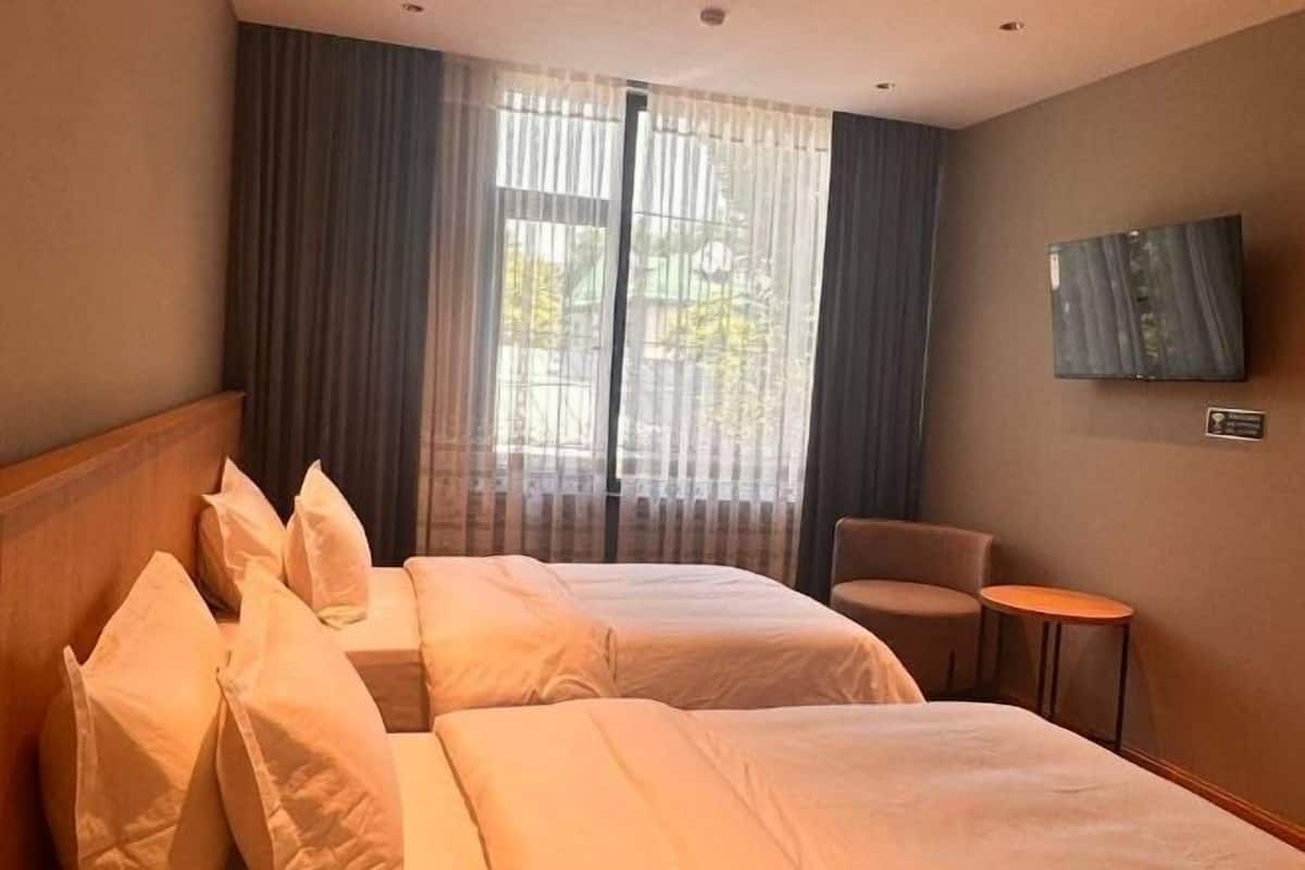 Une chambre d’hôtel avec deux lits, un téléviseur fixé au mur, une petite table et une chaise.