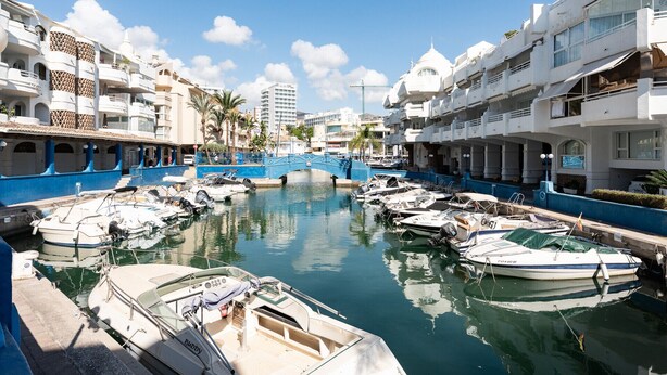 Un port de plaisance avec des bateaux amarrés, un pont bleu et des bâtiments blancs dotés de balcons.