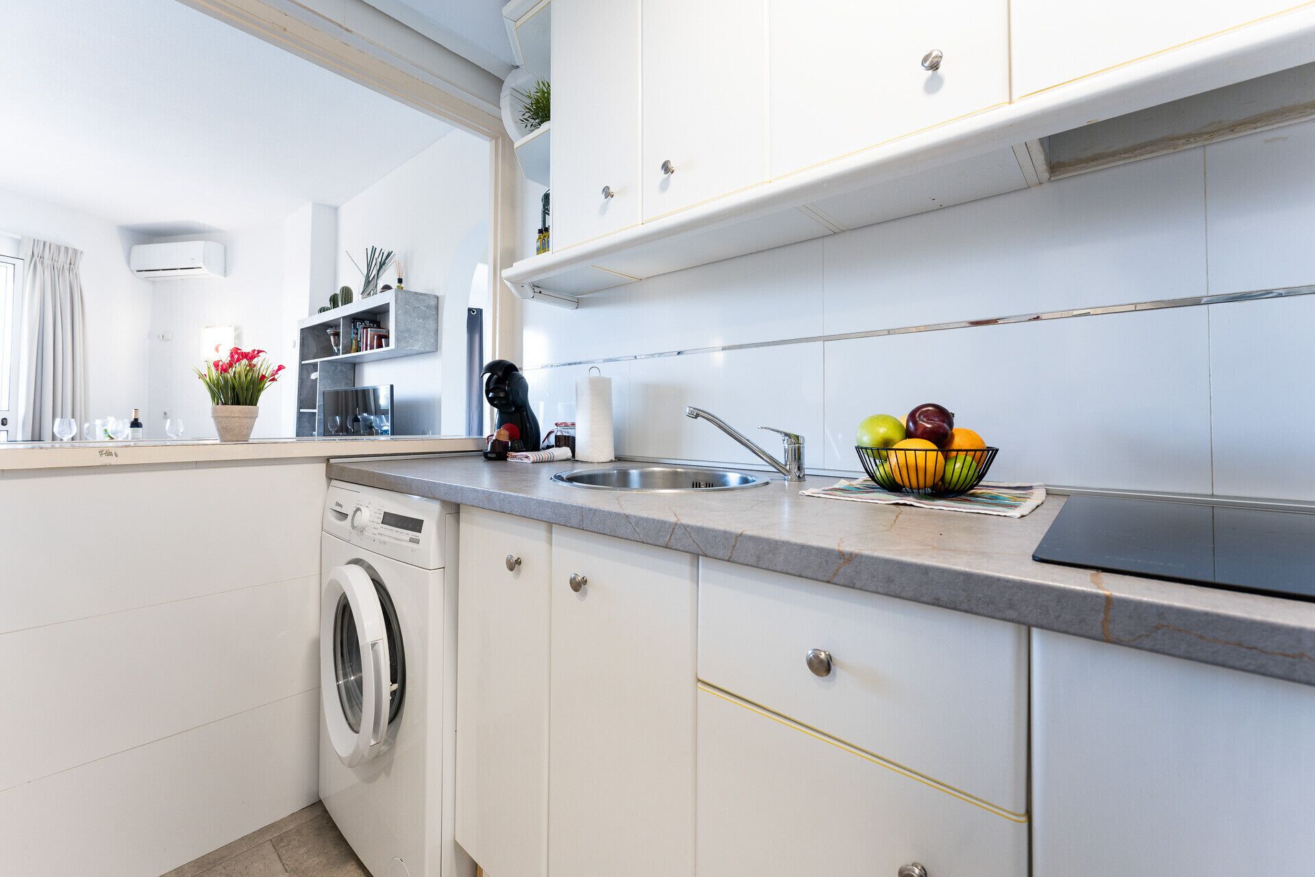 A modern kitchen with a built-in washing machine, a sink, and a fruit bowl on the counter.
