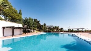 Une piscine d’eau cristalline, bordée de pergolas en bois, avec en arrière-plan la vue d’un bâtiment.
