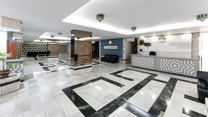 Un hall d’entrée spacieux avec un comptoir de réception, un mur bleu orné d’un tableau encadré et un sol à motifs géométriques.