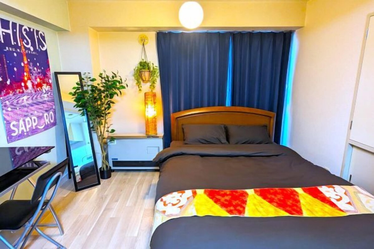 Una camera da letto con un letto, una scrivania, una sedia, una pianta in vaso e un quadro appeso al muro.