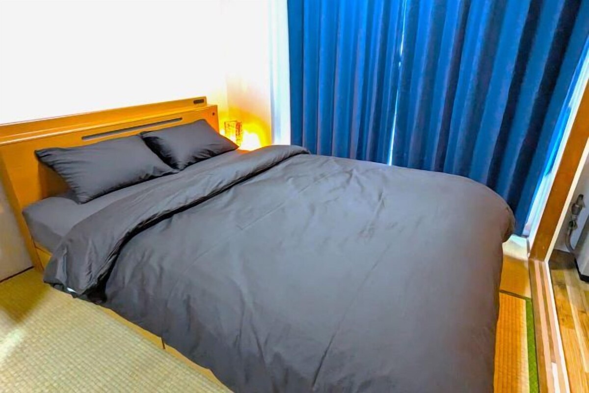 Un letto con testiera in legno, copripiumino scuro e una lampada sul comodino.