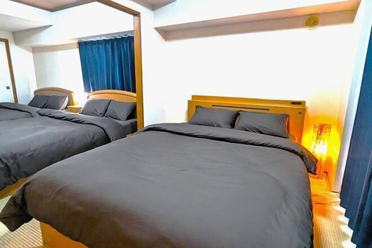 A hotel room with two single beds, a nightstand with a lamp, and a window with blue curtains.