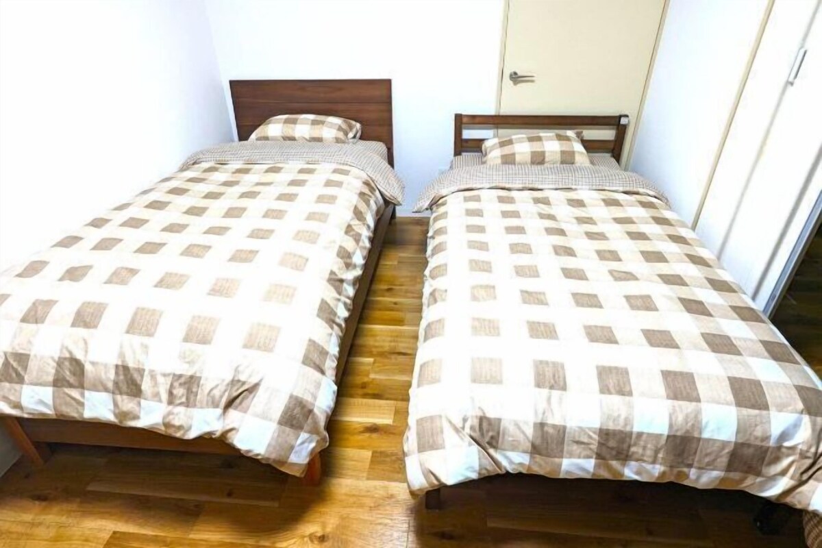 Two single beds with checkered bedding in a room with wooden flooring and a door in the background.
