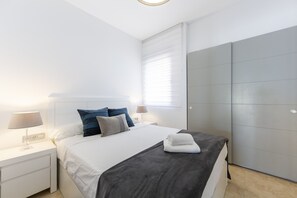 A modern bedroom with a bed, nightstands, a grey wardrobe, and a window with blinds. - Almería, Suite 344, Aralia (Vera)