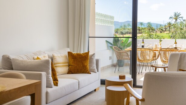 A modern living room with a sofa, a round wooden table, and a balcony with wicker chairs. - Almería, Suite 344, Aralia (Vera)